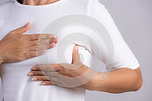 Woman hand checking lumps on her breast for signs of breast cancer on gray background. Healthcare concept