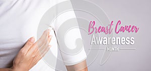 Woman hand checking lumps on her breast for signs of breast cancer on gray background. Healthcare concept
