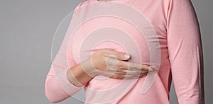 Woman hand checking lumps on her breast for signs of breast cancer on gray background. Healthcare concept