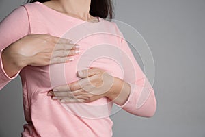 Woman hand checking lumps on her breast for signs of breast cancer on gray background. Healthcare concept photo