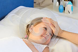 Woman hand on child forehead to feel temperature. Child in bed