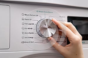 Woman hand choosing program on automatic washing machine for daily laundry at home