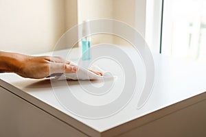 Woman hand cleaning headboard with disinfectant wet wipe and alcohol spray in bedroom at home. Concept of disinfecting surfaces