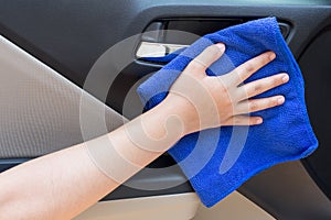 Woman hand cleaning interior car door panel with microfiber clot