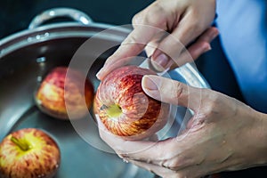 woman hand is cleaning red apple in bucket of water