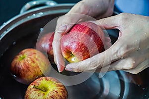 woman hand is cleaning red apple in bucket of water, closed up