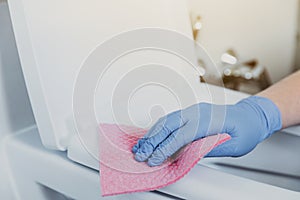 Woman hand cleaning toilet bowl, seat with detergent, pink cloth, wet wipe