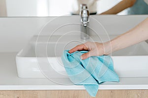 Woman hand cleaning washbasin with a blue cloth photo
