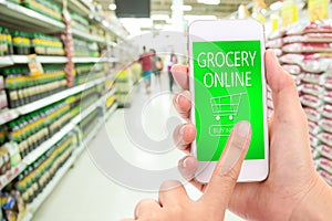 Woman hand click BUY NOW on mobile with blur supermarket background, Grocery online, delivery concept.