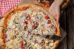 Woman hand close up holding pizza slice on a wooden table. Pizza delivery.