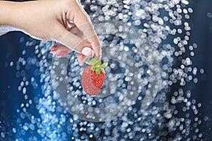 Woman hand close up holding red strawberry under drops of water. Girl showing red strawberry on a water background. Healthy lifest