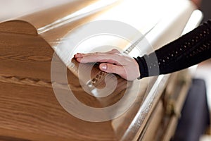 Woman hand on coffin lid at funeral in church