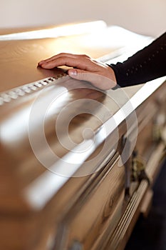 Woman hand on coffin lid at funeral in church