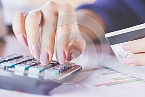 Woman hand counting on calculator using her credit card for shopping online