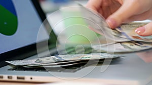 Woman hand counting dollar bills on laptop keyboard. . Online business money