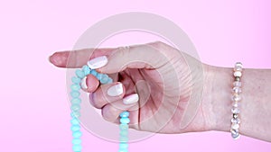 Woman hand counts mala beads strands of gemstones used for keeping count during mantra meditations. Pink background