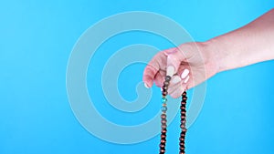 Woman hand counts mala beads strands used for keeping count during mantra meditations. Blue background. Spirituality