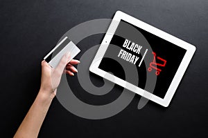 Woman hand with credit card and tablet with sign `Black Friday` over black background. Online shopping, black friday concept