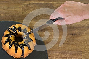 Woman hand is cutting a lemon cake with chocolate on a wooden ta