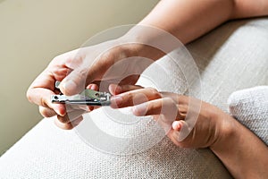 Woman hand cutting nails using nail clipper on sofa at living room