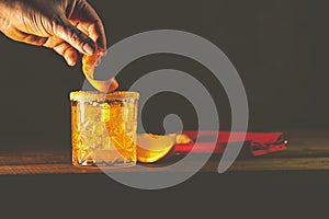 Woman hand decorate orange twist alcoholic cocktail negroni on old wooden board. Drink with gin, campari martini rosso and orange