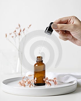 Woman hand dropping aroma oil to brown glass bottle with flask and dried flower background