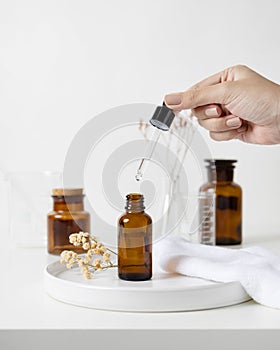 Woman hand dropping aroma oil to brown glass bottle with flask and dried flower background