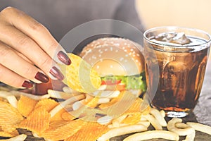 Woman hand eating fast food burger, potato chips,french fries and sweet drink on wooden table