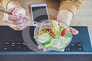 Woman hand eating healthy salad at desk while working on computer