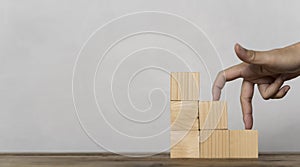 Woman hand finger walk on stacked wooden block like stairs, rises on the steps. Business development