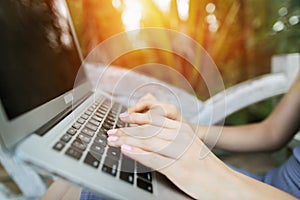 Woman hand fingers press laptop keyboard for remote work, background of sunshine green palms in Thailand, Phuket travel