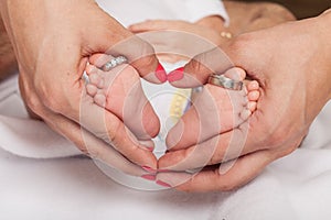 Woman hand forming heart around the foot of a baby with wedding rings parents