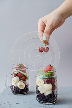 Woman hand with Fresh sliced fruit in a jar: strawberry, cherry