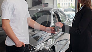 Woman hand gives a car keys to man hand in the car dealership close up. Unrecognized auto seller and a woman who bought