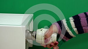 Woman Hand with glove Adjusting Temperature Of Radiator Thermostat on green.