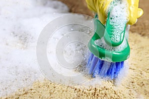 Woman hand in glove cleans carpet in the room, using brush. Close up. Cleaning concept