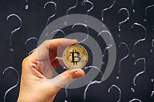 Woman hand with golden Bitcoin against blackboard with question