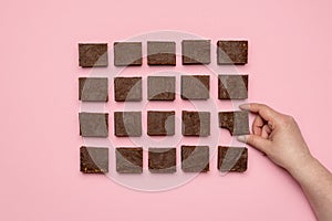 Woman hand grabbing a piece of fudge. Chocolate fudge on pink background top view