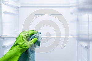 Woman hand in green glove clean glass refrigerator shelf