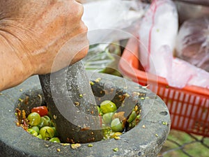 Woman hand is grinding chili and tomatoes by granite mortar