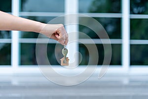 A woman hand is handing over a key with a key ring house in the background of a modern house. Concept of home sales-lease, New hou