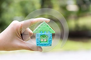 Woman hand hold home block with blur green background Concept for dream home, family fulfillment