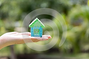 Woman hand hold home block model with blur green background Concept for dream home, family fulfillment