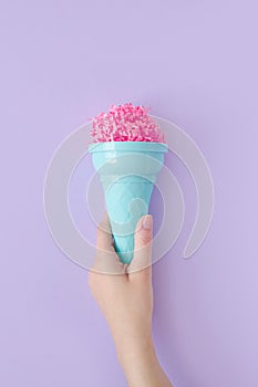 Woman hand hold pink paper ice cream scoop with ice cream plastic cone on pastel purple background. Minimal summer