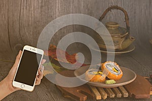 Woman hand hold smart phone on blurred japanese sushi set