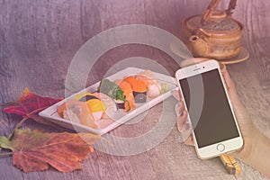 Woman hand hold smart phone on blurred japanese sushi set