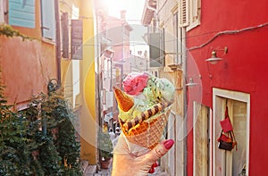 Woman hand hold sweet ice - cream cone with different flavors held in hand on the background of old street in Rovinj