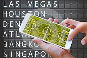 woman hand hold and touch screen smart phone or cellphone with football field on screen city name board photo