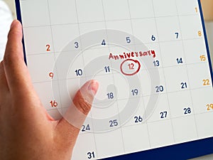 Woman hand hold white calendar written red circle and Anniversary word marked on white calendar. This Anniversary marker to remind