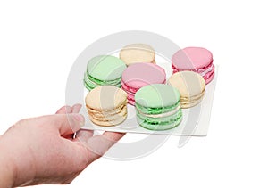 Woman hand holdin a white plate with colored sweet macaroons, fr